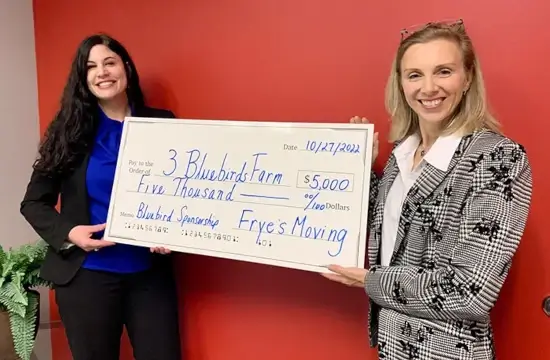 Two ladies from Bluebirds Farms holding novelty donation check of $5000 from Frye's Moving Company sponsorship
