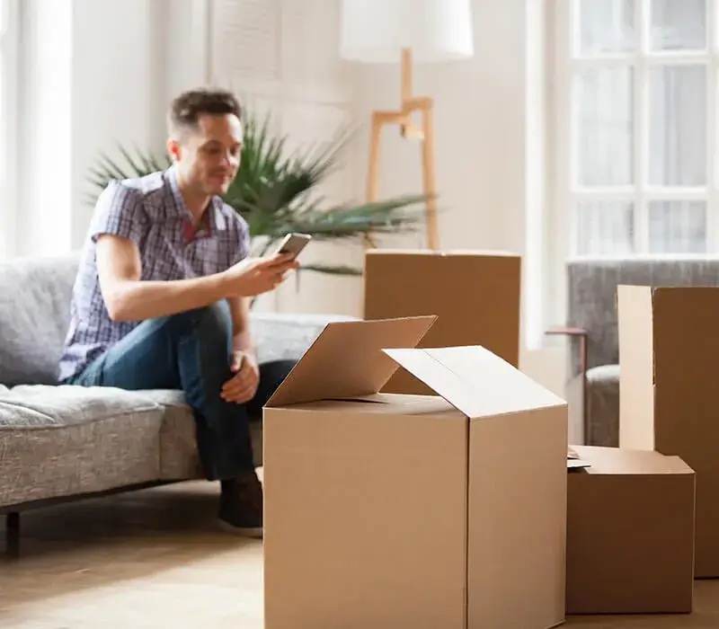 Man using phone, unpacking boxes in new apartment.