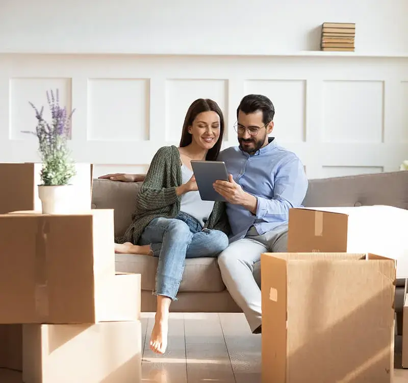 Couple planning move with tablet among boxes in living room.