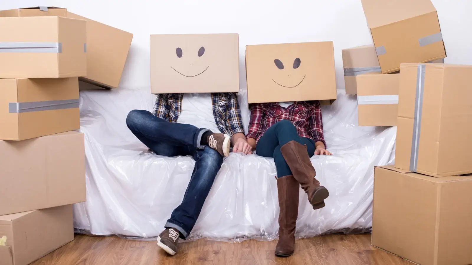Couple with cardboard box heads sitting among moving boxes.
