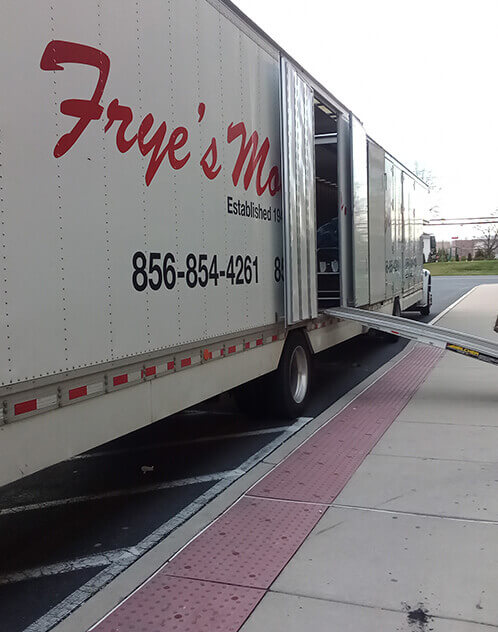 Side view of Frye's Moving truck with company phone number (856) 854-4261 and open ramp on urban road.
