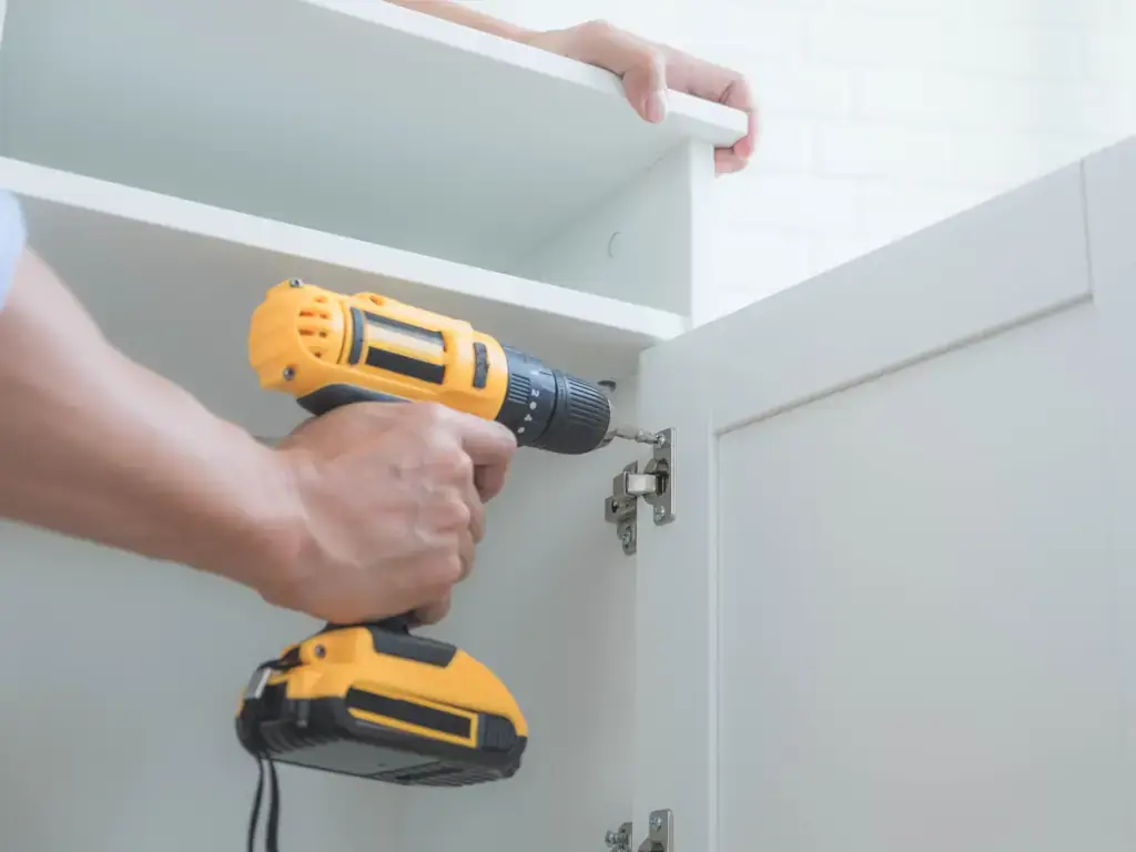 Furniture assembly Man using a power drill to attach a cabinet door to a piece of furniture.