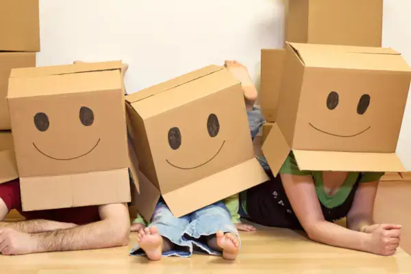 Silly parents and toddler posing with cardboard boxes on their heads with smiley faces written on the boxes in black marker.