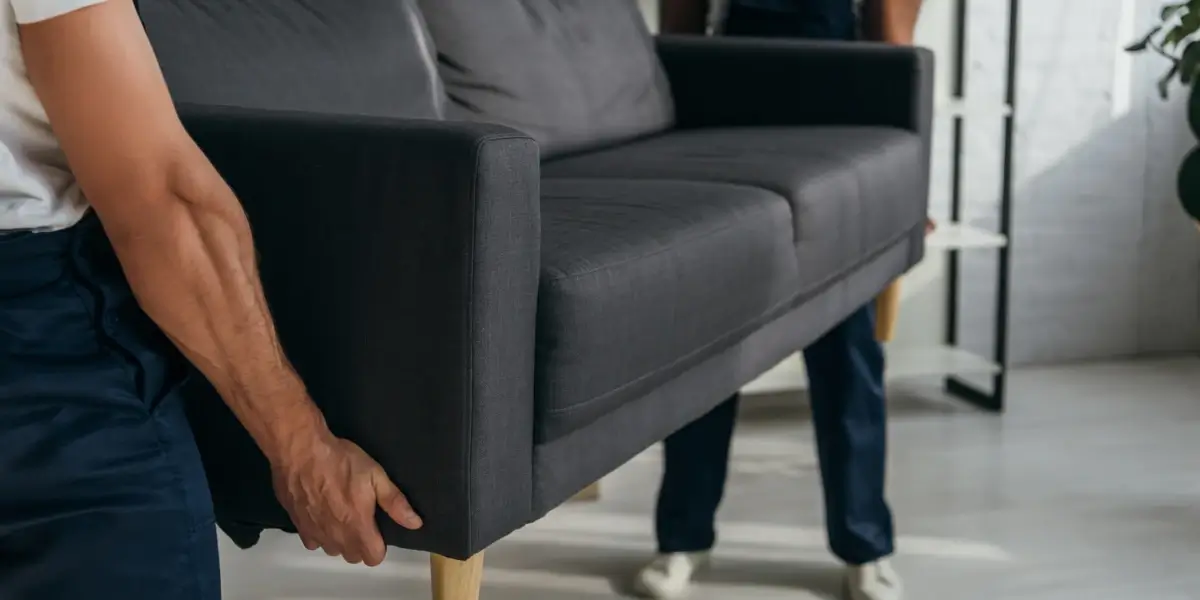 Two people lifting a gray sofa in living room.