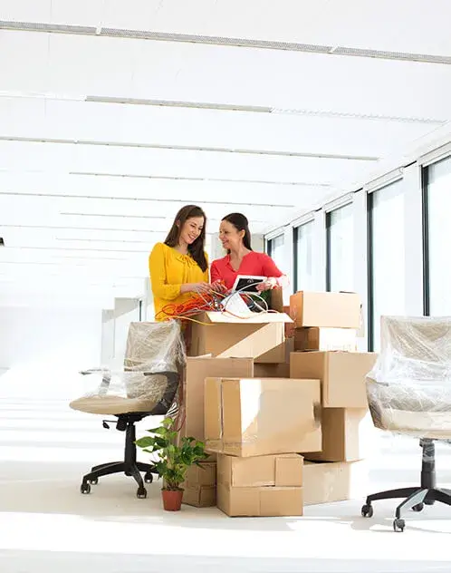 Two women unpacking boxes in a bright office space.