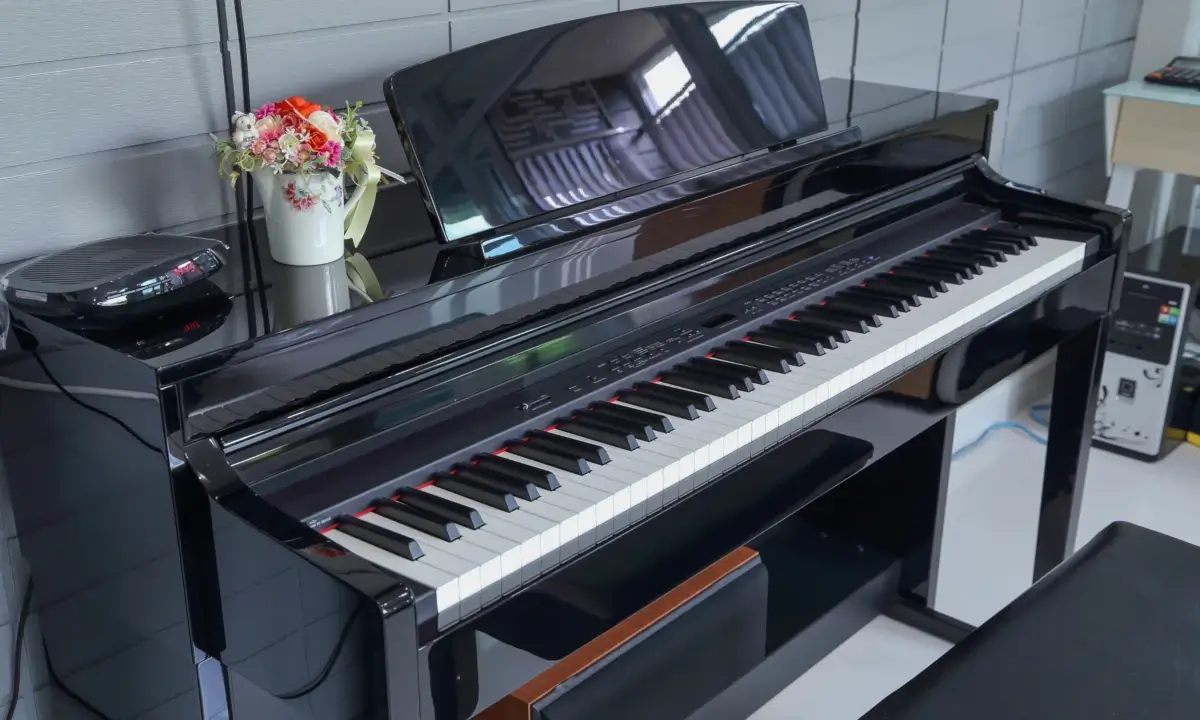 Black digital piano with a vase of flowers.